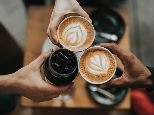 Masada iki fincan latte ve bir soğuk kahve tutan eller